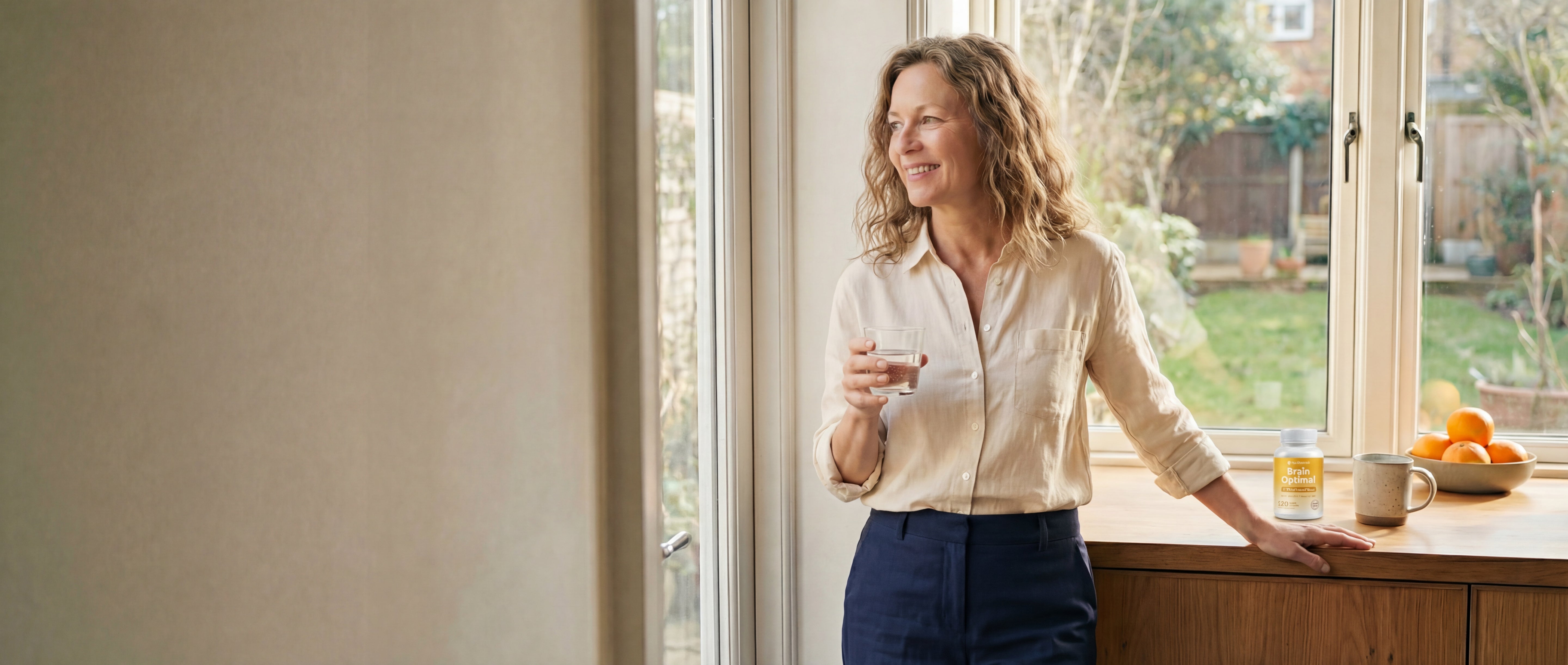 Woman standing by a window in a home, holding a glass of water.